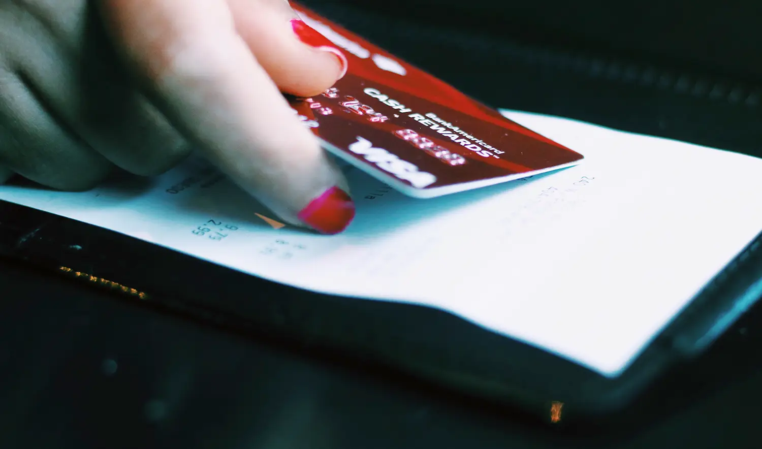 A woman's hand holding a credit card over a credit card receipt